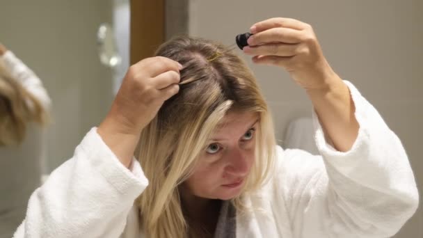 Vrouw brengt olie aan op haar haar met pipet. Schoonheidsverzorging voor hoofdhuid en haar. Schoonheidsbehandeling thuis. - Video