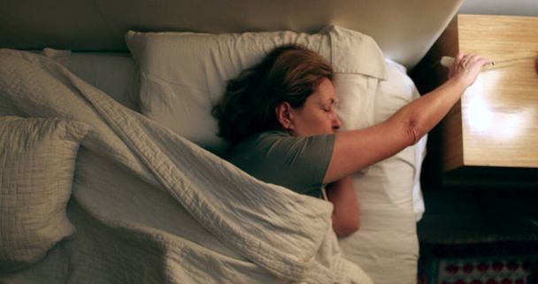 Senior woman resting in bed turning light off - Foto, imagen