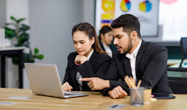 Millennial Asian Indian professional successful bearded male businessman mentor pointing coaching helping female businesswoman employee colleague in formal business suit working via laptop computer. - Photo, Image