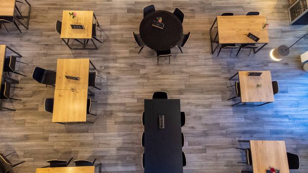 Una perspectiva de arriba hacia abajo captura el diseño de mesas y sillas dentro de un restaurante. Los muebles cuidadosamente arreglados establecen el escenario para una experiencia de comedor acogedora. Mesas y sillas de restaurante de arriba hacia abajo - Foto, Imagen