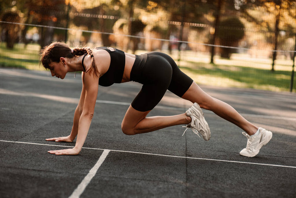 A young girl with an athletic figure is doing fitness at the sports ground. fitness trainer. Slim body. Healthy lifestyle. Sportswoman doing a workout. High quality photo - Photo, Image