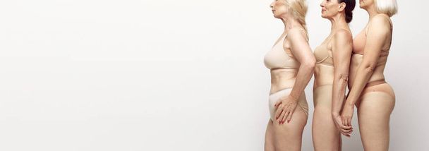 Cropped side view image of female bodies in underwear against grey studio background. Natural body of senior women. Concept of age, natural beauty. body and skin care, healthy lifestyle. Banner - Photo, Image