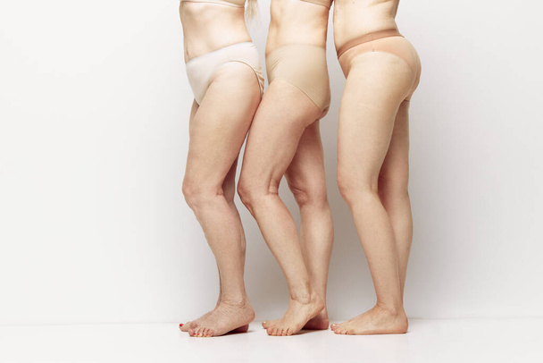 Cropped side view image of female legs in underwear against grey studio background. Natural body of senior women. Concept of age, natural beauty. body and skin care, healthy lifestyle - 写真・画像