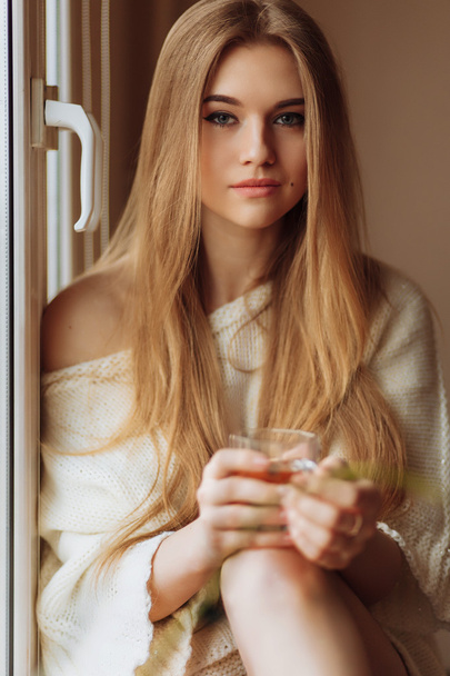 Beautiful blond woman drinking tea in the morning sitting by the window - Photo, image