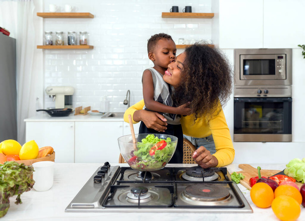 Mère et fils joyeux préparent des aliments frais et nutritifs dans une cuisine ensoleillée, incarnant des liens familiaux sains et une vie saine. - Photo, image