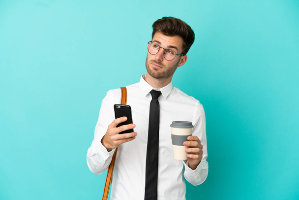 Hombre de negocios sobre fondo aislado sosteniendo café para llevar y un móvil mientras piensa algo - Foto, Imagen