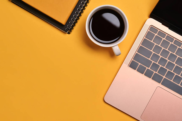 Ένα φλιτζάνι καφέ, σημειωματάριο και laptop σε κίτρινο φόντο. Κάτοψη με χώρο αντιγραφής. - Φωτογραφία, εικόνα
