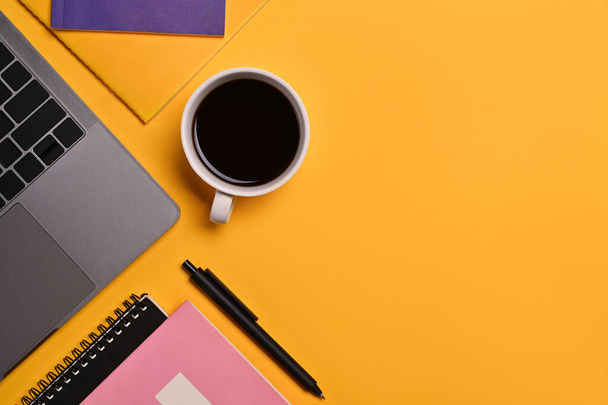Een kopje koffie, laptop, notitieboekje en pen op gele achtergrond. Bovenaanzicht met ruimte voor tekst. - Foto, afbeelding