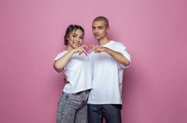 Beyaz tişörtlü genç bir kadın ve adam parlak pembe stüdyo duvarında duruyor. - Fotoğraf, Görsel