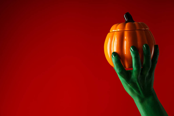 Pumpkin in green hand on red background, space for text - Photo, Image