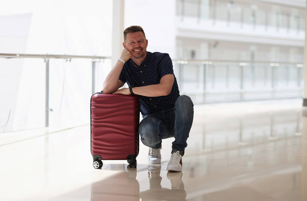 Happy smiling man is sitting suitcase. Cheerful traveler man ready for vacation - Foto, Imagem