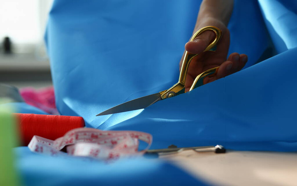 Woman hands cut blue fabric with tailor scissors closeup. Tailor in atelier and tailoring - Φωτογραφία, εικόνα