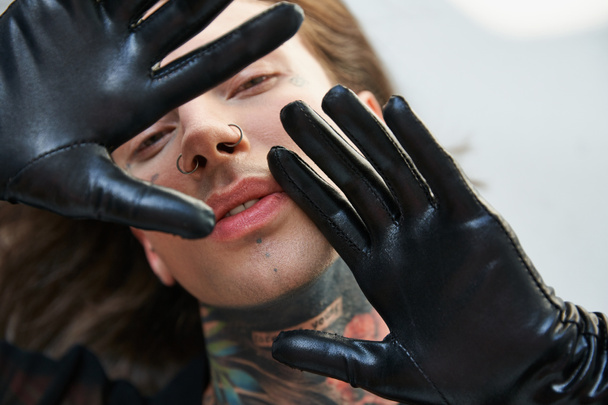 beau jeune homme en tenue noire avec piercing et tatouages regardant la caméra, concept de mode - Photo, image