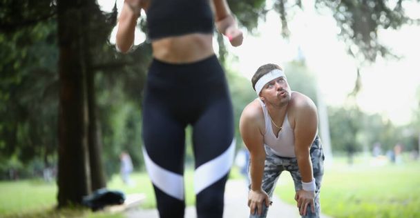 Спортивная девушка и измученный спортсмен стоят на заднем плане. Усталость лени и потеря мотивации в тренировках - Фото, изображение