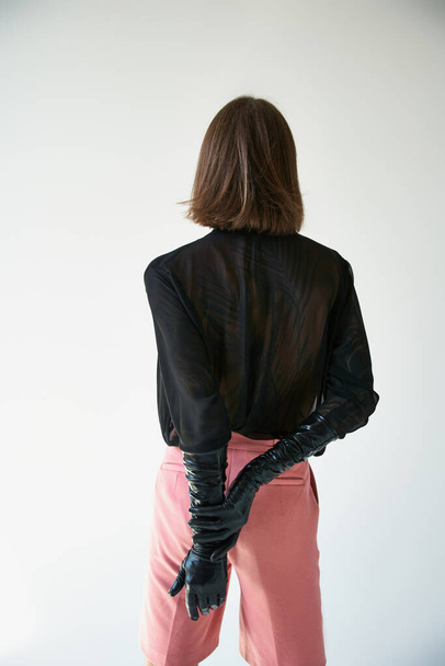 visão traseira do jovem homem de cabelos longos em luvas de couro elegantes e calças de moda rosa, conceito de moda - Foto, Imagem