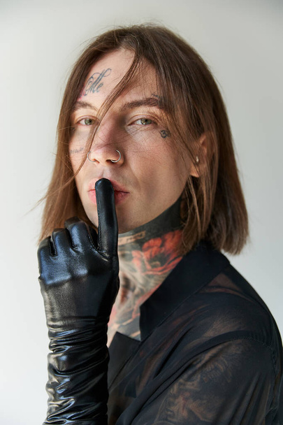 vertical shot of handsome man with black gloves looking at camera showing silence gesture, fashion - Fotografie, Obrázek