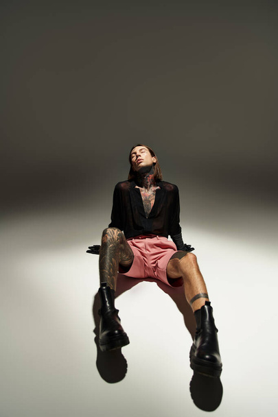 vertical shot of stylish male model in alluring outfit sitting on floor with closed eyes, fashion - Photo, Image