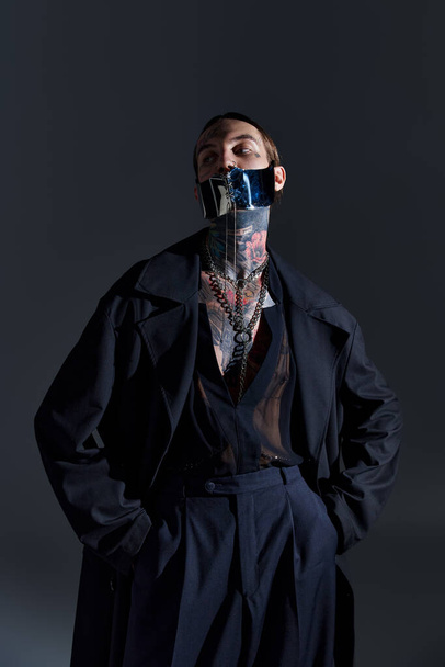 good looking man with tattoos in laced stylish mask posing on black backdrop, fashion concept - Photo, image