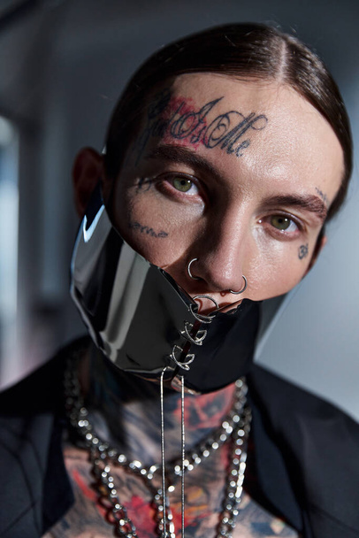 портрет молодого стильного чоловіка з татуюваннями в футуристичній масці, що дивиться на камеру, концепція моди - Фото, зображення