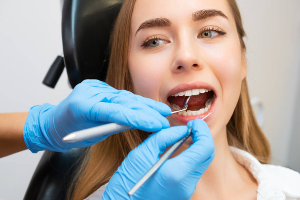 歯科クリニックで歯科手術中に椅子に座っている女性患者. 歯科医はミラーツールの助けを借りて前歯をチェックし,歯の強さをチェックします - 写真・画像