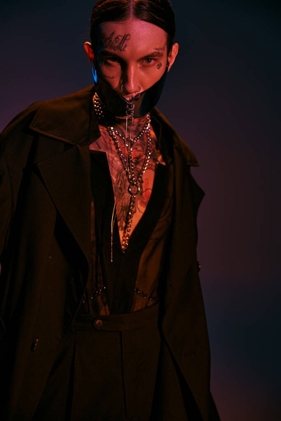 handsome young man with tattoos in black futuristic attire looking at camera, fashion concept - Foto, immagini