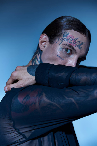 vertical shot of alluring man with tattoos on face in transparent stylish shirt looking at camera - Foto, Imagen