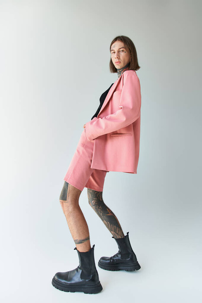 young stylish male model in pink blazer and shorts bending his body slightly and looking at camera - Fotografie, Obrázek