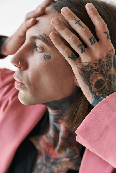 portrait of young fashionable man with tattoos on face and piercing with hands on face looking away - Foto, afbeelding