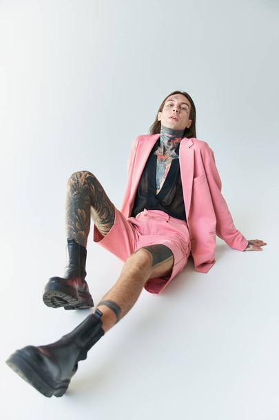 tiro vertical de un joven guapo en blazer rosa y pantalones cortos sentados en el suelo, concepto de moda - Foto, Imagen