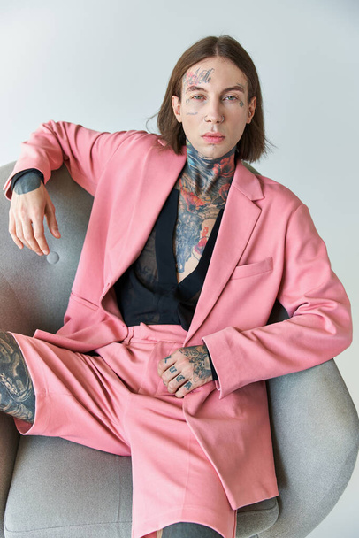 stylish sexy man in pink blazer and shorts sitting on chair looking at camera, fashion concept - Фото, изображение