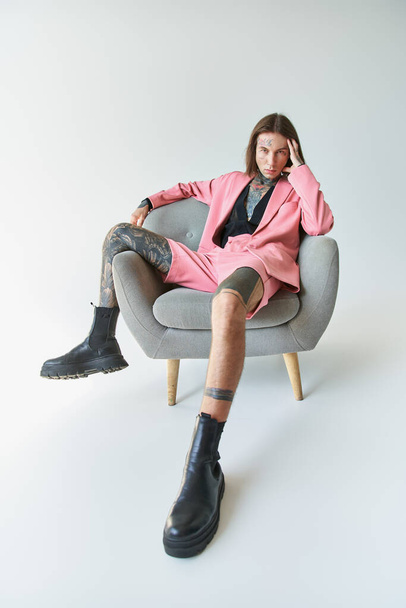 jóképű fiatalember elegáns rózsaszín blézer és alacsony ül a széken nézi a kamera, divat - Fotó, kép