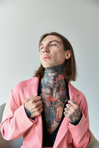 vertical shot of sexy young man with tattoos touching collar of his stylish pink blazer, fashion - Valokuva, kuva