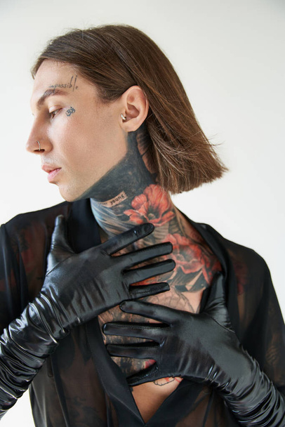 tiro vertical de hombre joven con tatuajes y piercing posando de perfil con las manos en el cuello, la moda - Foto, Imagen