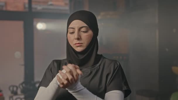Arc lövés magabiztos fiatal muszlim nő fekete hidzsáb bemelegítő kezek és csuklók, miközben készül a boksz edzés - Felvétel, videó