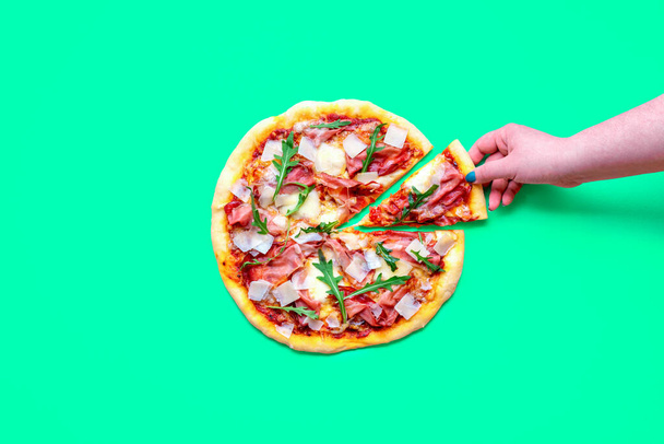Bovenaanzicht met een zelfgemaakte ham pizza geïsoleerd op een groene achtergrond. Vrouwenhand neemt een stuk pizza - Foto, afbeelding