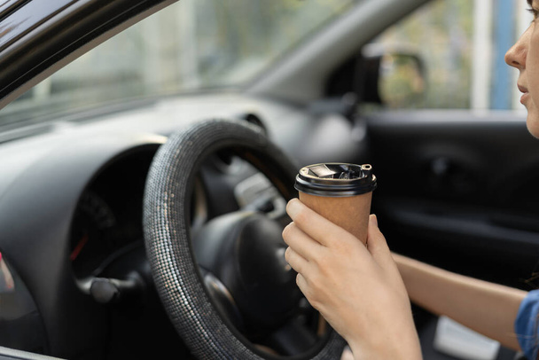 Primo piano di mani femminili che tengono una tazza di caffè e un volante. Autista donna con caffè caldo al volante. Copia spazio - Foto, immagini