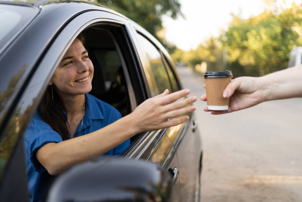 Schöne Millennial-Frau, die Auto fährt und glücklich Kaffee mitnimmt. Kopierraum - Foto, Bild