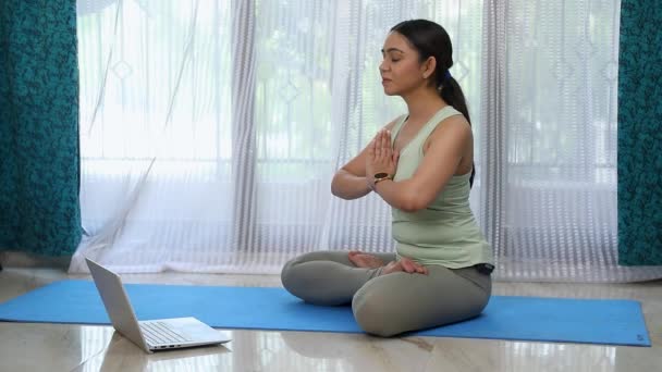 Video Yoga and meditation at home. Woman performing gyan mudra, sitting on mat in front of laptop - Footage, Video