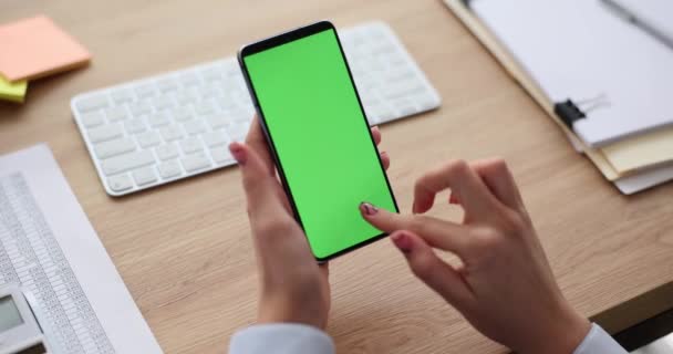 Büroangestellte scrollt soziale Medien auf Smartphone mit grünem Bildschirm. Büroangestellte mit Maniküre sitzt im Büro gegen Tastatur am Holztisch in Zeitlupe - Filmmaterial, Video