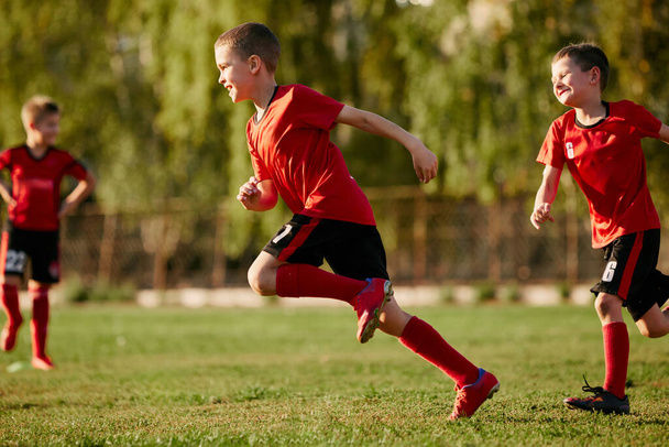 Full length side view portrait of kid, football player in sport uniform training, running at speed in motion before match on soccer field. Concept of sport inventory, workout, leisure activity. Ad - Photo, Image