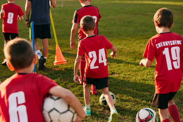 Back view photo of kids, football players in sport uniform preparing for training, in motion with balls before match on soccer field. Concept of sport inventory, workout, leisure activity. Ad - Photo, image