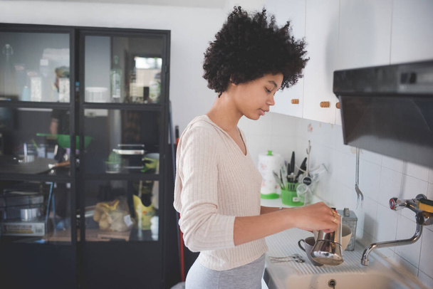 Молода багатоетнічна жінка вдома готує каву за допомогою кави  - Фото, зображення