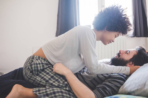 Νεαρό πολυεθνικό ζευγάρι αγκαλιάζει υπνοδωμάτιο φορώντας πιτζάμες - Φωτογραφία, εικόνα