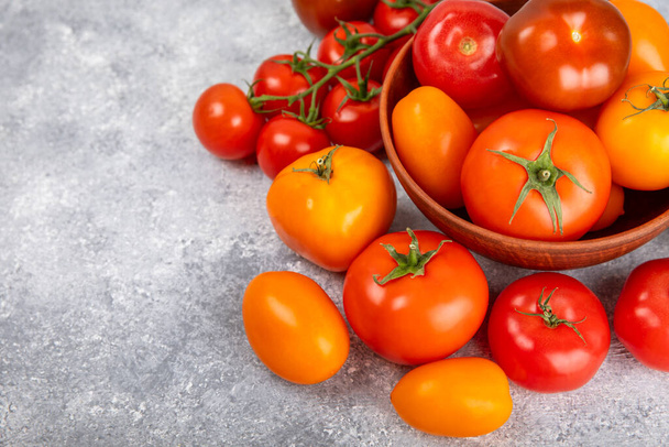 大理石のテクスチャの背景にトマト。チェリートマト、黄色、ピンク、茶色、黒のトマトをボウルに入れます。有機野菜、収穫。ビーガン。新鮮な熟したトマト。コピースペース. - 写真・画像