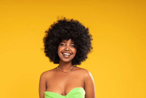 Beauty Girl with delicate natural Makeup smiling to the camera. Glamour young woman with afro hairstyle. Yellow studio background. Copy space. Real people emotions. - Φωτογραφία, εικόνα