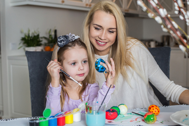 Young mother and her beautiful daughter painting Easter eggs - Fotoğraf, Görsel