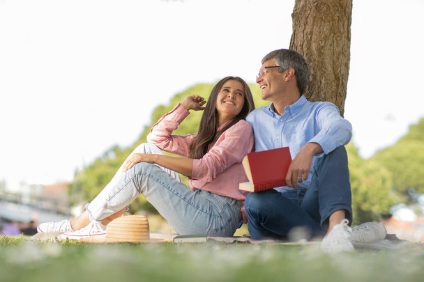 Venkovní volný čas. Šťastní starší manželé čtení knihy, zatímco relaxovat společně v parku, usmívající se muž středního věku a žena sedí na kostkované pod stromem, těší čas s sebou, kopírovat prostor - Fotografie, Obrázek