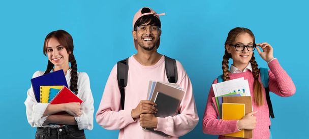 Gruppe fröhlicher junger multiethnischer Studenten mit Rucksäcken und Arbeitsbüchern, die vor blauem Studiohintergrund posieren, vielseitige glückliche College-Freunde, die vor buntem Hintergrund stehen, in die Kamera lächeln, Collage - Foto, Bild