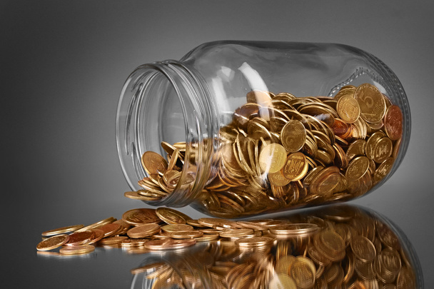 Coins spilling from a money jar on gray background - Φωτογραφία, εικόνα