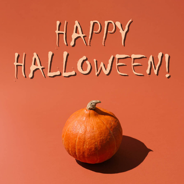 Minimalny pomysł estetyczny z listami Happy Halloween. Jesienna koncepcja monochromatyczna ze świeżą dynią na pomarańczowym tle. - Zdjęcie, obraz